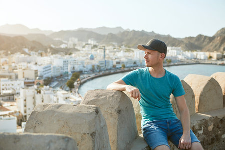 Traveler in Muscat. Young man against old city, sea and mountain range in Oman.