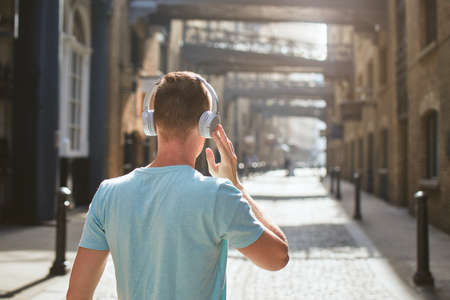 Young man with headphones listening music against old city street at morning light. London, United Kingdom.の写真素材