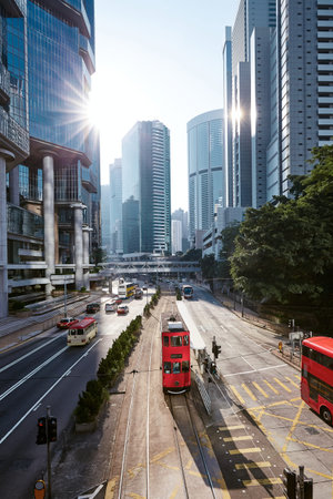 Red double-decker tram on city street against skyscrapers. Traffic in downtown financial area in...