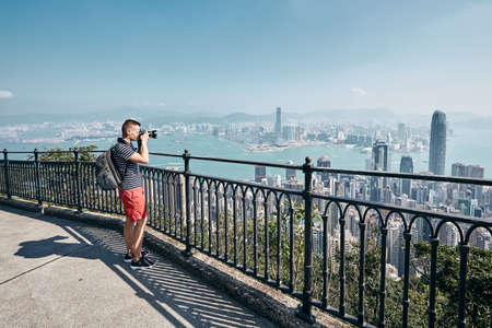 Young man (traveler) with backpack photographing urban skyline. Victoria Peak, Hong Kong.の写真素材