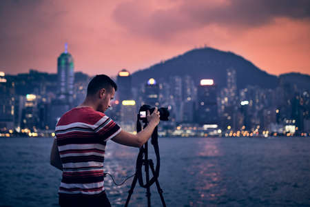 Young photographer (traveler) with tripod photographing urban skyline at sunset, Hong Kong.の写真素材
