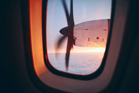 View from window of propeller airplane during flight above clouds at beautiful sunrice. Selective focus on turboprop engine.の写真素材