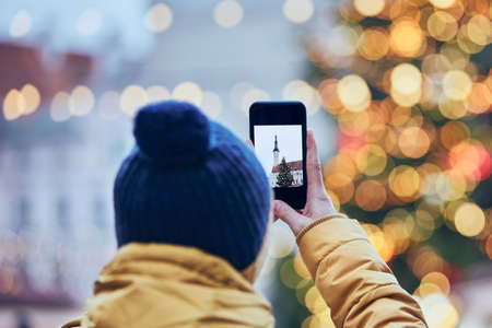 Man with smart phone photographing Christmas tree against Town Hall in Tallinn, Estonia.の写真素材