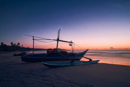 Seascape at colorful dawn. Fishing boat on sand beach, Sri Lankaの写真素材