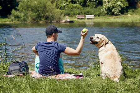 Summertime relaxation with dog. Young man playing with his labrador retriver on riverside. の写真素材