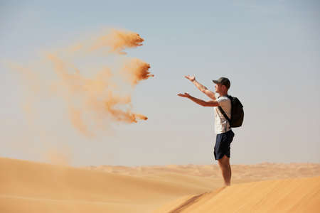 Happy traveler in desert. Young man throwing sand in wind. Abu Dhabi, United Arab Emiratesの写真素材