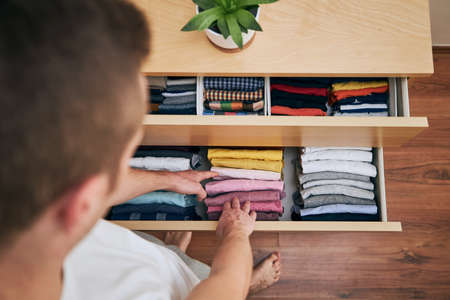 Organizing and cleaning home. Man preparing orderly folded t-shirts in drawer.の写真素材
