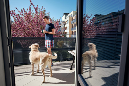 Spring morning at home. Young man with his labrador retriever on balcony.
