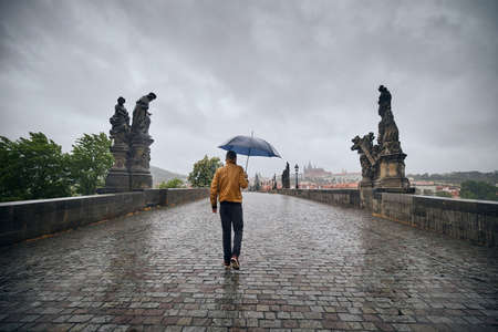 Lonely man with umbrella in heavy rain walking on empty Charles Bridge. Prague Czech Republicの写真素材