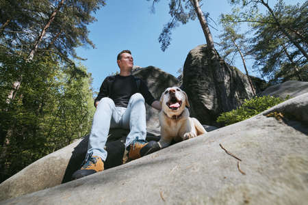 Man with his dog resting on rock in the middle of forest. Bohemian Paradise, Czech Republicの写真素材