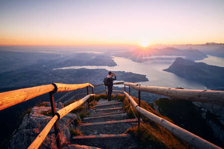 Man photographing landscape with lake and mountains at beautiful sunrise. View from Mount Pilatus, Lucerne, Switzerlandの写真素材