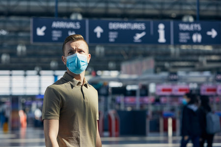 Man wearing face mask against airport check-in counter. Themes travel in new normal, coronavirus and personal protection.の写真素材