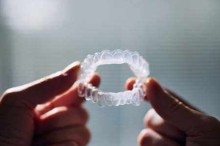 Close-up view of hand holding teeth whitening trays against window.の写真素材