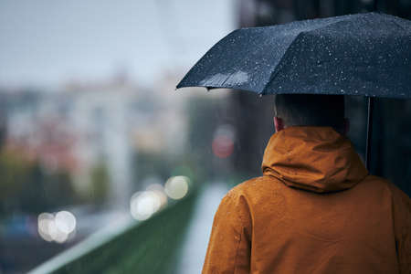 Young man with umbrella is walking on bridge during heavy rain. Gloomy day in Prague, Czech Republicの写真素材