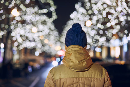 Christmas holiday in city. Rear view of young man against illuminated street with shops. Prague, Czech Republic.の写真素材