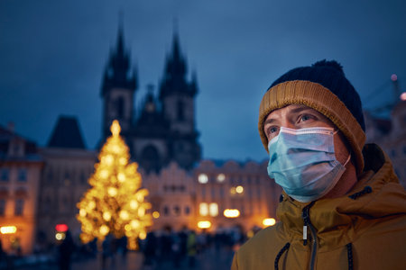 Young man with face mask against Christmas tree in Prague. Themes coronavirus pandemic during Christmas holiday and personal responsibility.の写真素材