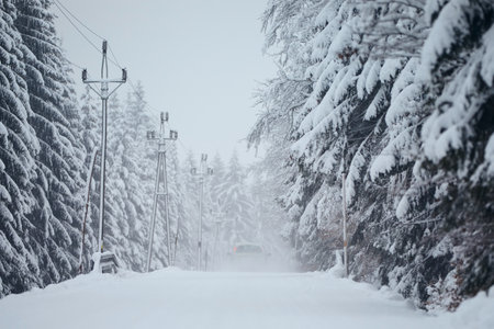 Transportation during winter weather. Car driving on snow covered road in the middle of forest during snowing.の写真素材