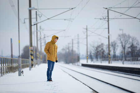 Snowy railroad station during frosty day. Man standing on platform and waiting for delayed train.の写真素材