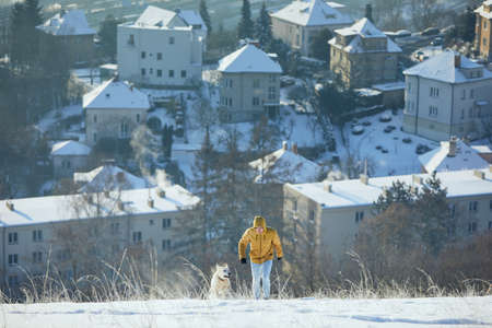 Happy young man with dog in winter. Pet owner with his labrador retriever walking in snow against city. Prague, Czech Republicの写真素材