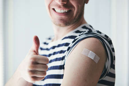 Happy young man showing thumb up and his arm after vaccination. Themes prevention, vaccine and health care during pandemicの写真素材