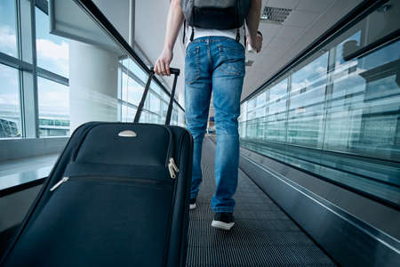 Man walking with suitcase. Rear view of traveler on moving walkway at airport terminal.の写真素材