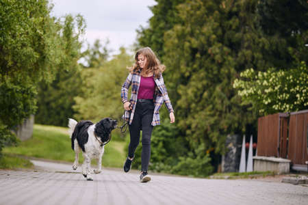 Happy young girl running with her dog on pet leash down street.の写真素材