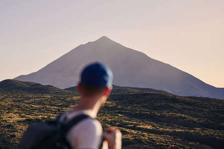 Traveler against landscape with Pico de Teide at dusk. Young man with backpack looking on volcano. Tenerife, Canary Islands, Spain.の写真素材
