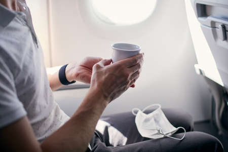 Passenger with face mask drinking coffee in airplane. Themes traveling during pandemic covid-19.の写真素材