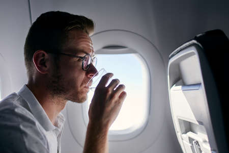 Portrait of passenger during flight. Young man drinking water from plastic cup.の写真素材