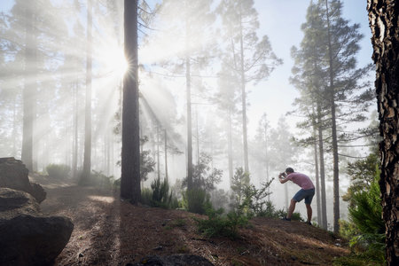 Photographer in foggy forest. Young man during photographing trees in beautiful light. Tenerife,...
