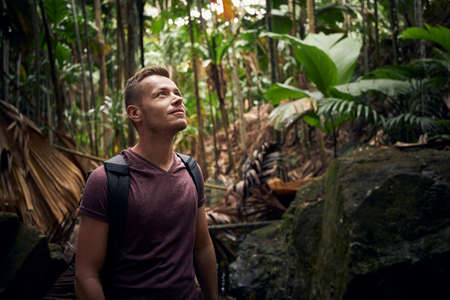 Young man with backpack discovering jungle. Traveler in tropical rainforest in Seychelles.の写真素材