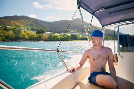 Man enjoying travel on bow of motorboat against beautiful coast of Praslin Island in Seychelles.の写真素材