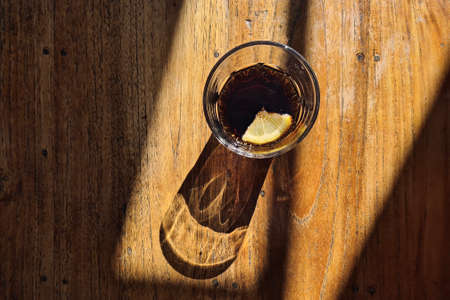 Drinking glass with cola drink. Light and shadow on wooden table.の写真素材