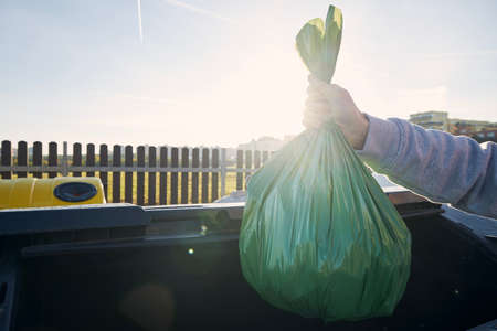 Man walking with rubbish. Hand carrying plastic bag against garbage cans on street.の写真素材