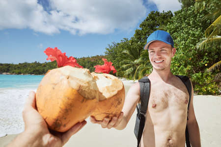 Friends drinking coconut drink together on white sand beach against beautiful coastline of tropical island. Anze Lazio, Seychelles.の写真素材