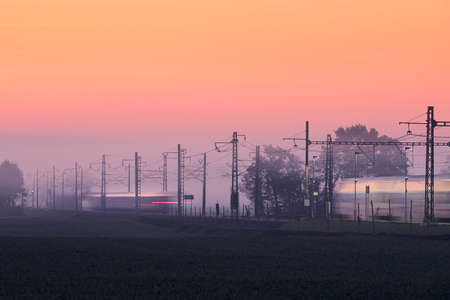 Traffic on electrified railroad track at foggy autumn morning. Trains in blurred motion.の写真素材