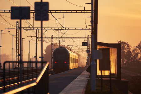 Railway at sunrise. Passenger train leaving railroad station.の写真素材