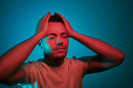 Portrait illuminated of neon lighting. Adult man in red and green lights have head in hands.の写真素材