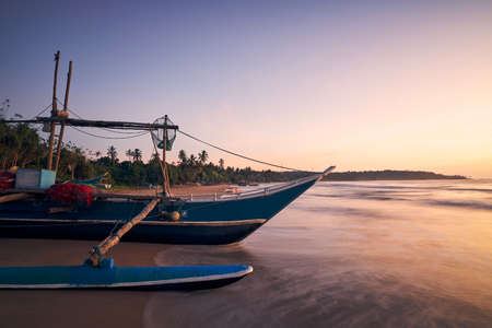Fishing boat on sand beach at colorful dawn. Coastline near Tangalle in Sri Lankaの写真素材