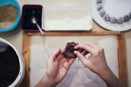 Hands holding cocoa dough and raisin on background work table with other ingredients. Preparation of...