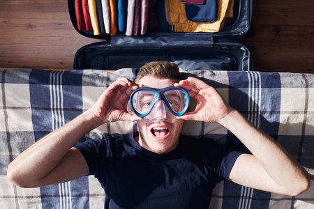 Crazy portrait of happy young man during packing suitcase and planning travel adventure.の写真素材