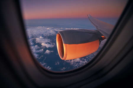 View from window of airplane during flight above ocean at beautiful sunrise. Selective focus on jet engine.の写真素材