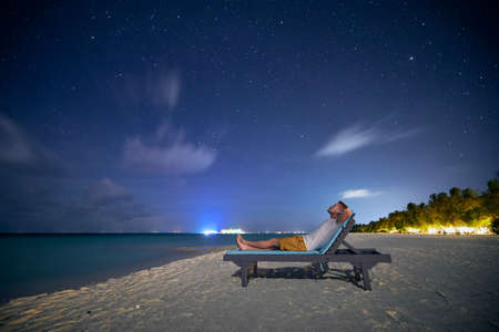 Man lying on sunbed on sand beach and looking up to stars on night sky.の写真素材