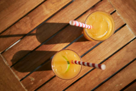 Two refreshing cold drinks. Glasses of cocktails with ice and fresh fruits on wooden table.の写真素材