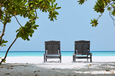 Rear view on two empty wooden deckchairs on idyllic sand beach against sea with turquoise water.の写真素材