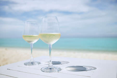 Two wineglass with white wine on wooden table against idyllic beach and turquoise sea.の写真素材