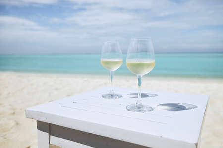 Two wineglass with white wine on wooden table against idyllic beach and turquoise sea.の写真素材