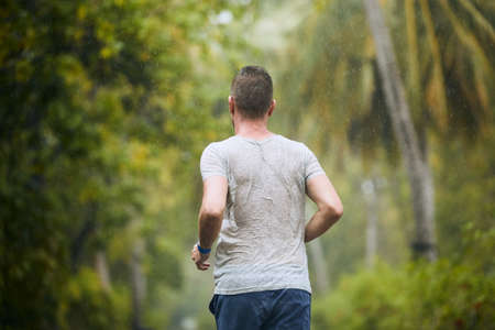 Rear view of runner in heavy rain. Drenched young man runing in nature.の写真素材