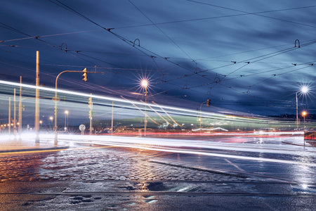 Light trails of trams and cars in Prague downtown. Busy road intersection in city at rainy evening.