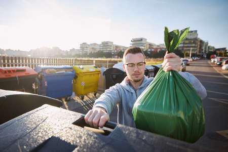 Man walking with rubbish. Front view of person throwing plastic bag to garbage can on city street.の写真素材
